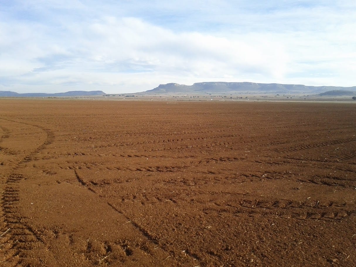 Campo agrícola arado y vacío, tierra roja, con mesetas al fondo